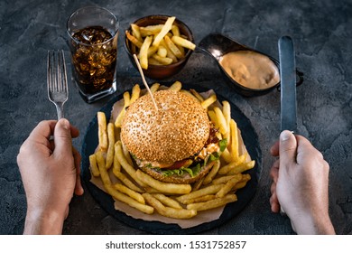 Male Hands Holding Fork And Knife Above Burger