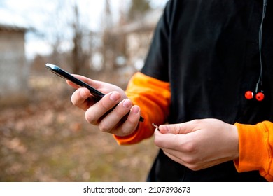 Male Hands Holding Smartphone And Earphones Plug After Active Exercise Outdoors. Monitoring Health Tracker App During Sports Activity On The Phone. Closeup