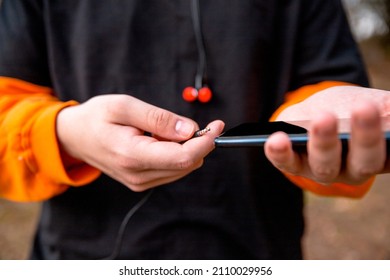 Male Hands Holding Smartphone And Earphones Plug After Active Exercise Outdoors. Monitoring Health Tracker App During Sports Activity On The Phone. Close Up