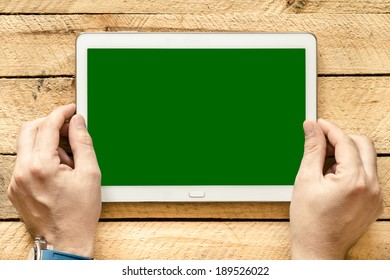 Male Hands Holding Tablet Pc With Green Empty Screen On Wooden Background