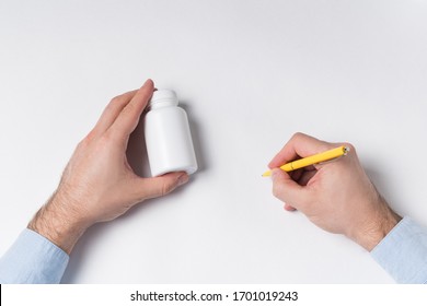 Male Hands Holds Pill Bottle And Pen. Doctor Writes Prescription Concept. Top View.