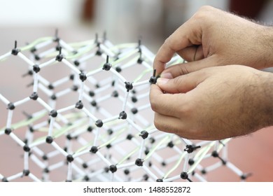 Male hands joining together a lab molecular structure made of black and white plastic pieces.
