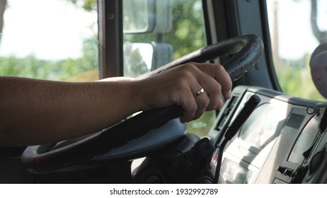 Male hands of lorry driver holds a big steering wheel while riding a truck through countryside. Trucker driving to destination at country road. Logistics and transportation concept. Slow motion.