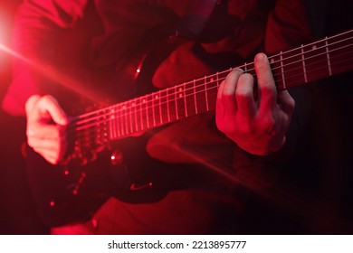 Male Hands Playing Electric Guitar, Fingers Plucking Strings. Musician Man With Black Guitar At A Rock Concert Lighting Red Spotlight, Stage Show. Shot For Performance Poster, Music Cover