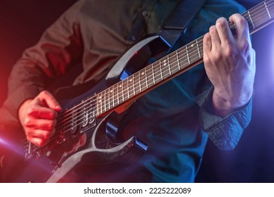 Male Hands Playing Electric Guitar, Fingers Plucking Strings. Musician Man With A Black Guitar. Musical Instrument Lighting Red And Blue Spotlight, Stage Show. Shot For Performance Poster, Music Cover