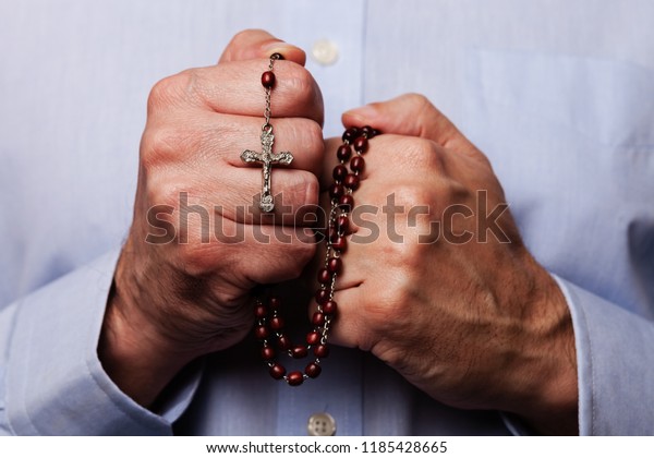 Male hands praying holding a beads rosary\
with Jesus Christ in the cross or Crucifix on black background.\
Mature man with Christian Catholic religious\
faith