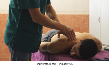 Male hands of professional masseur massaging shoulder of athlete lying on massage table in parlor. Arms of massagist doing health rubdown of back to muscular sportsman in salon. Close up Slow motion - Shutterstock ID 1483045925
