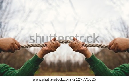 Male Hands pulling the rope in opposite directions outside. Two men same hands dragging rope on different sides in rivalry conflict. Copy space on white
