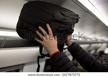Male hands put a black backpack on the top berth in a train while traveling. Storage space above the seats of public transport under the ceiling