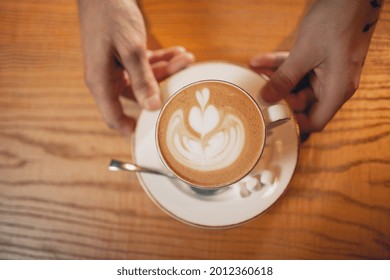 Male hands putting coffee in a big white cup, latte or cappuchino with lush milk froth and marshmallow on wooden table. View from above