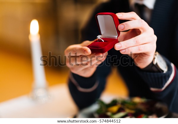 Male hands with red velvet box containing\
engagement ring with\
brilliant