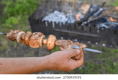 Male hands skillfully threading chunks of meat and mushrooms onto metal skewer. ingredients ready for grilling. preparation of preparing shashlik. man arranging marinated meat on a skewer. 