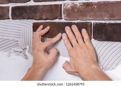 Male Hands, Soiled With A Building Mixture, Laying Decorative Stone On Plastered Wall. Repair Work, Renovation And Interior Design Concept