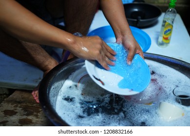 Male hands with sponge in foam wash dish in the ground local traditional wash dish style. 