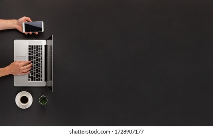 Male Hands Typing On Laptop And Using Smartphone At The Same Time On Abstract Dark Black Office Desk With Cup Of Coffe And Huge Copy Space