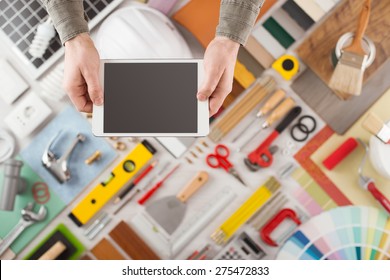 Male Hands Using A Digital Tablet, Construction And Home Decoration Tools On Background, Top View, DIY And Home Improvement Mobile App Concept