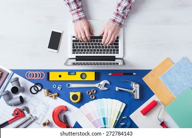 Male hands using a laptop next to plumbing work tools, tiles and swatches, online booking and home plumber service - Powered by Shutterstock