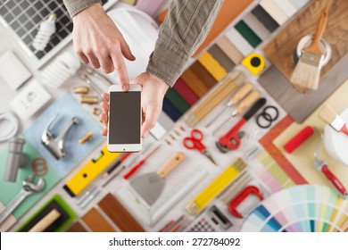 Male Hands Using A Touch Screen Smart Phone, Build And Home Renovation Tools On Background, Top View