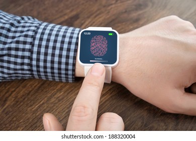 male hands with white smartwatch with a fingerprint on the screen over a wooden table 