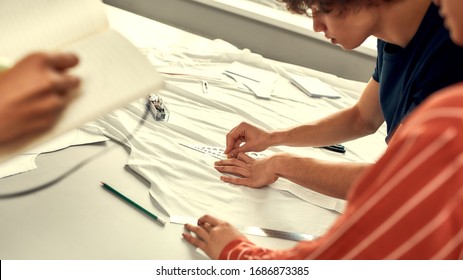 Male hands working with sketches or patterns at studio and preparing fabric. Group of millennials creating clothes together. T-shirt production concept. Horizontal shot. Web Banner - Powered by Shutterstock