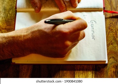 Male Hands Writing A Gratitude List In A Hardback Journal With An Ink Pen