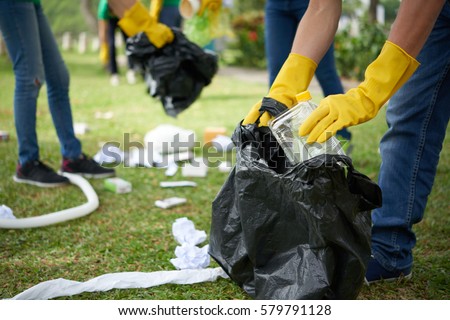 Male hands in yellow rubber gloves putting household waste into small bin bag