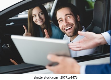 Male Handsome Caucasian Shop Assistant Showing Explaining To Family Couple Clients Customers Car Options Information On Digital Tablet Before Buying Choosing New Car Auto