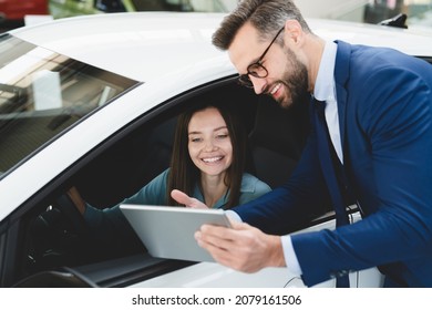Male handsome caucasian shop assistant showing explaining to a female client customer car options information on digital tablet before buying choosing new car auto