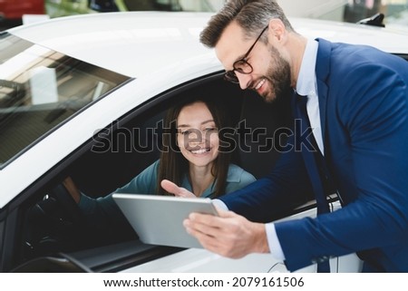 Male handsome caucasian shop assistant showing explaining to a female client customer car options information on digital tablet before buying choosing new car auto