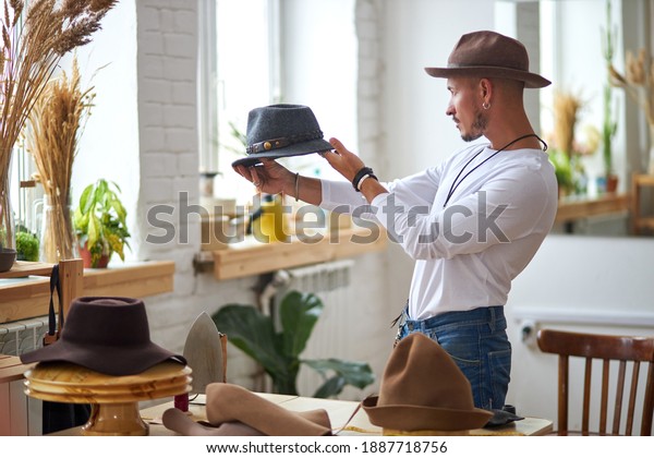 male hats maker standing at his atelier\
workshop, holding perfectly made hat for customers. successful\
adult business man employed at his own\
business