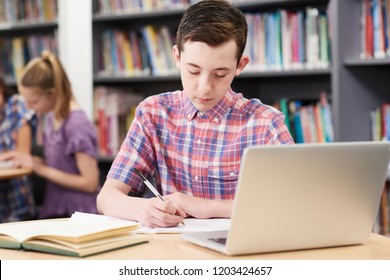 Male High School Student Working At Laptop In Library