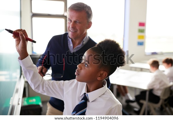 Male High School\
Teacher With Female Student Wearing Uniform Using Interactive\
Whiteboard During Lesson