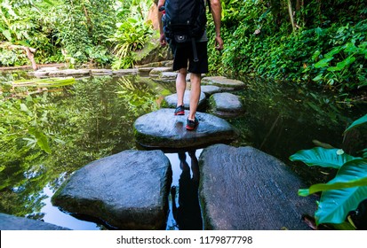 Male Hiker With Backpack Crossing A River On Stones.