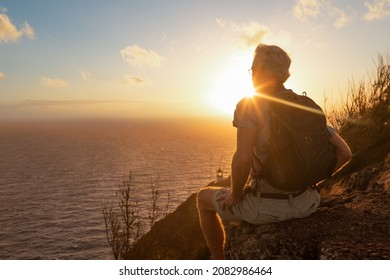 Male hiker with backpack sitting on a mountain cliff by the sea enjoying the beauty of nature. - Powered by Shutterstock