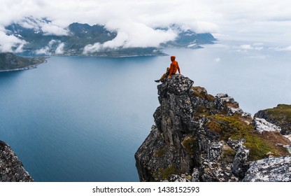 Male Hiker Celebrating Success On Top Of A Mountain And Looking To A Valley. Travel Man Alone On The Edge Cliff In Mountains Above Fjord Hiking Adventure 