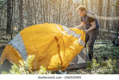 Male hiker is setting up a bright orange tent in the forest. Concept of tourism, hiking and staying in nature.