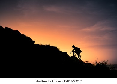 Male Hiker Silhouette Climbing Up The Edge Of A Mountain. 