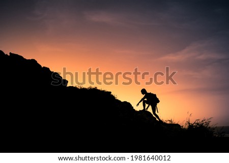 Male hiker silhouette climbing up the edge of a mountain. 