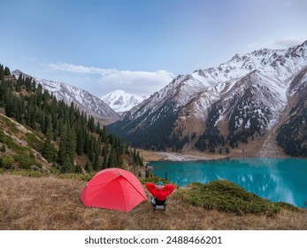 A male hiker sitting on a folding chair near a tent in a high mountainous area. He enjoys a magnificent panoramic view of snow-capped peaks and a turquoise mountain lake - Powered by Shutterstock