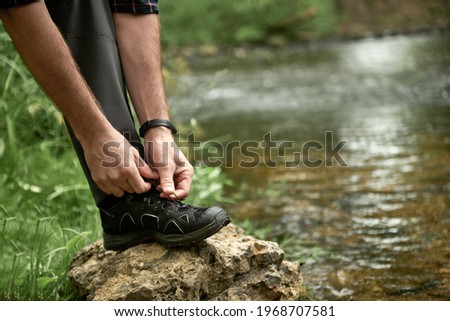 Male hiker tying shoelaces placing his foot on a large stone by the stream, while trekking outdoors, shallow debth of field, selective focus. The concept of comfortable hiking shoes. Stock photo © 