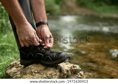 Male hiker tying shoelaces placing his foot on a large stone by the creek, while trekking outdoors, shallow debth of field, selective focus. The concept of comfortable hiking shoes Stock photo © 