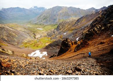 Male hiker walks in Tombstone Territorial Park, Yukon Canada. Huge stunning mountains and a lake is in the distance. Inspiring landscape. Summer and Fall hiking. Campground with tents.