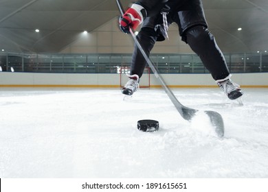 Male hockey player in sports uniform, gloves and skates moving down rink in front of camera against stadium environment while going to shoot puck - Powered by Shutterstock