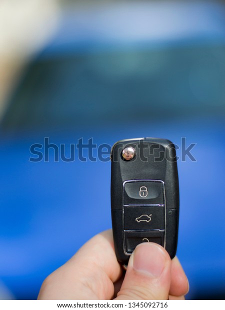 male holding car key (remote control) in\
hands on blur blue car\
background.