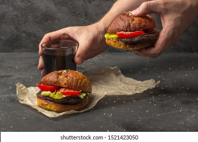 Male Holding Freshly Prepared Grilled Beef Burger Above A Dark Background. Man Serves Burger To The Table. American Snack Close Up.