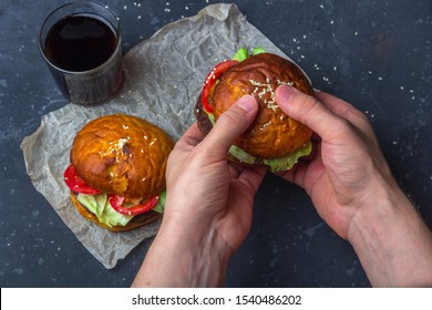 Male Holding Freshly Prepared Grilled Beef Burger Above A Dark Background. Man Serves Burger To The Table. American Snack Close Up.