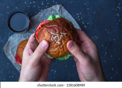 Male Holding Freshly Prepared Grilled Beef Burger Above A Dark Background. Man Serves Burger To The Table. American Snack Close Up.