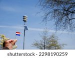 Male holding Netherland flag with in background pole of acoustic air alarm system also known as air raid siren alert aka luchtalarm in Dutch in Holland to warn public for example during war or attack