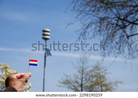 Male holding Netherland flag with in background pole of acoustic air alarm system also known as air raid siren alert aka luchtalarm in Dutch in Holland to warn public for example during war or attack