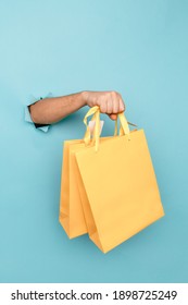 Male holds in hand paper bag for purchases through a hole in blue paper